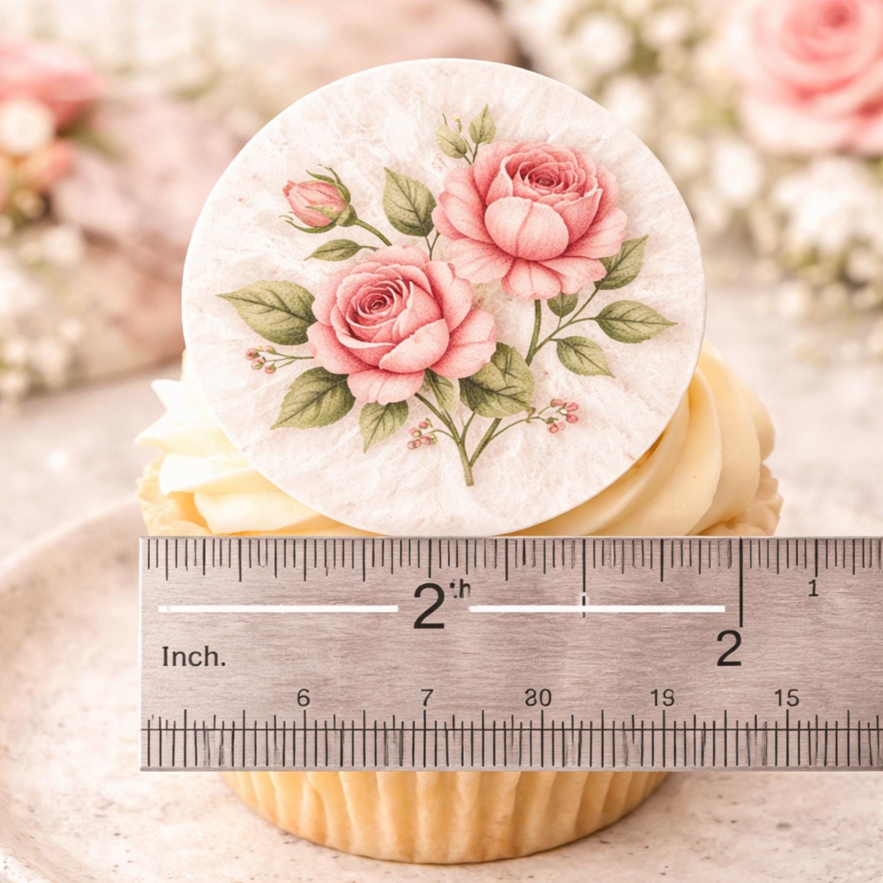 A cupcake topped with a round edible image featuring pink roses and green leaves. The edible image measures approximately 2 inches in diameter. The cupcake has a yellow base and white frosting.